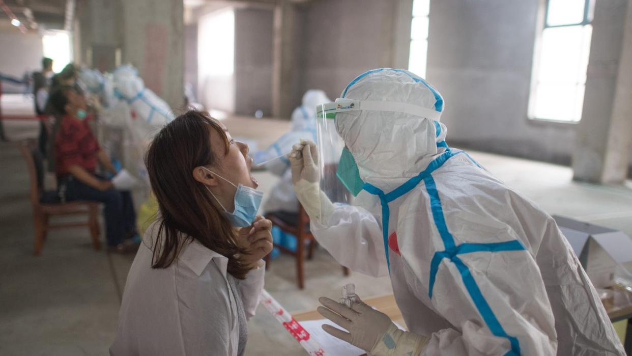 Eine Frau wird in Wuhan von einer Person in Schutzanzug auf das Coronavirus getestet. Wissenschaftler haben in der chinesischen Metropole Freiwilligen den Wirkstoff Ad5-nCoV verabreicht und berichten von ersten Erfolgen.