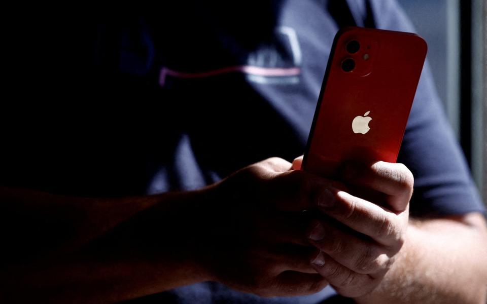 A man poses with an Apple iPhone 12 at a mobile phone store.