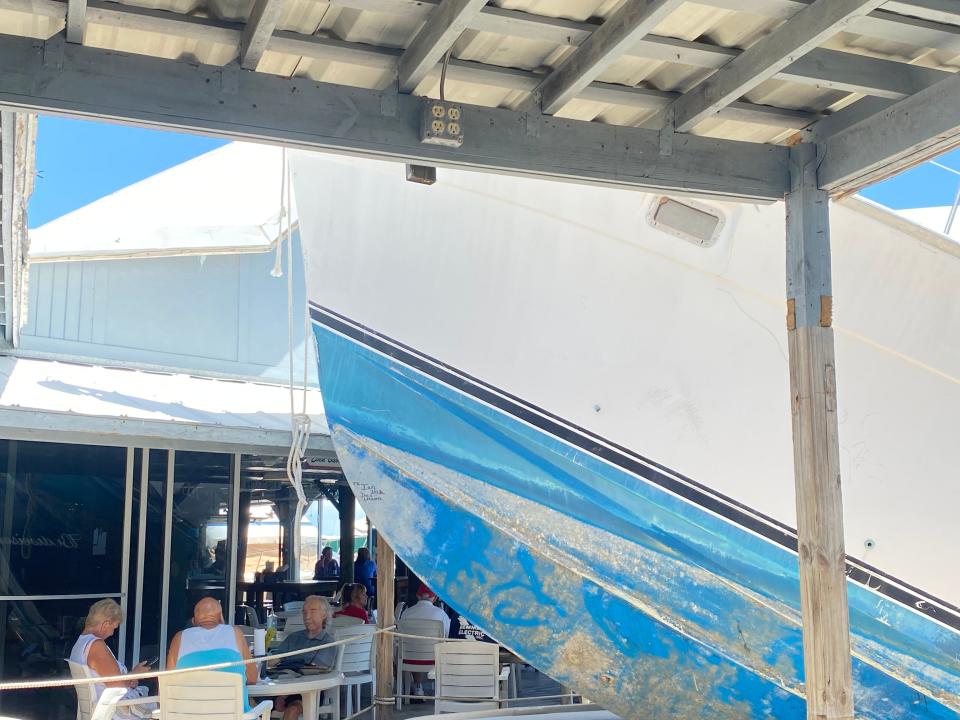 Tables and chairs at Bonita Bill's are set up near the giant boat that has been stuck to the dock since Sept. 28, 2022. Three people were having lunch on May 18, 2023.