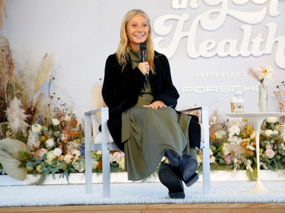 Paltrow sitting onstage with a microphone wearing a black sweater at a 'Goop in Health' event