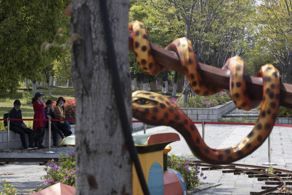 Residents removing their protective face masks briefly for a rest are seen near a snake-shaped lantern at a park in Wuhan, central China's Hubei province, Thursday, April 9, 2020. Released from their apartments after a 2 1/2-month quarantine, residents of the city where the coronavirus pandemic began are cautiously returning to shopping and strolling in the street but say they still go out little and keep children home while they wait for schools to reopen. (AP Photo/Ng Han Guan)