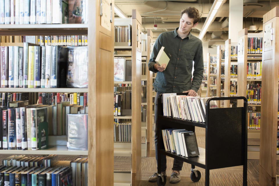 Person with a cart of books putting them on the shelves of a library