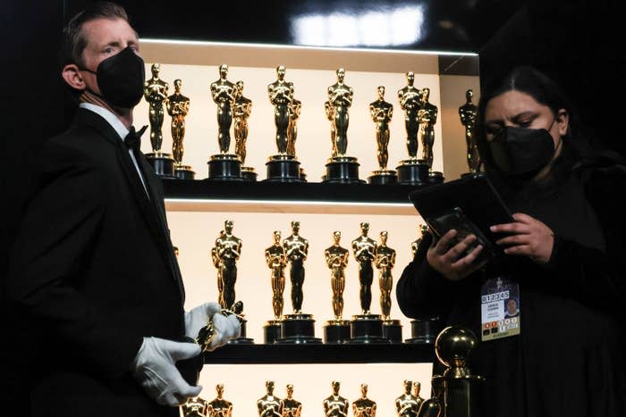 Two employees standing in front of shelves full of Oscar statuettes