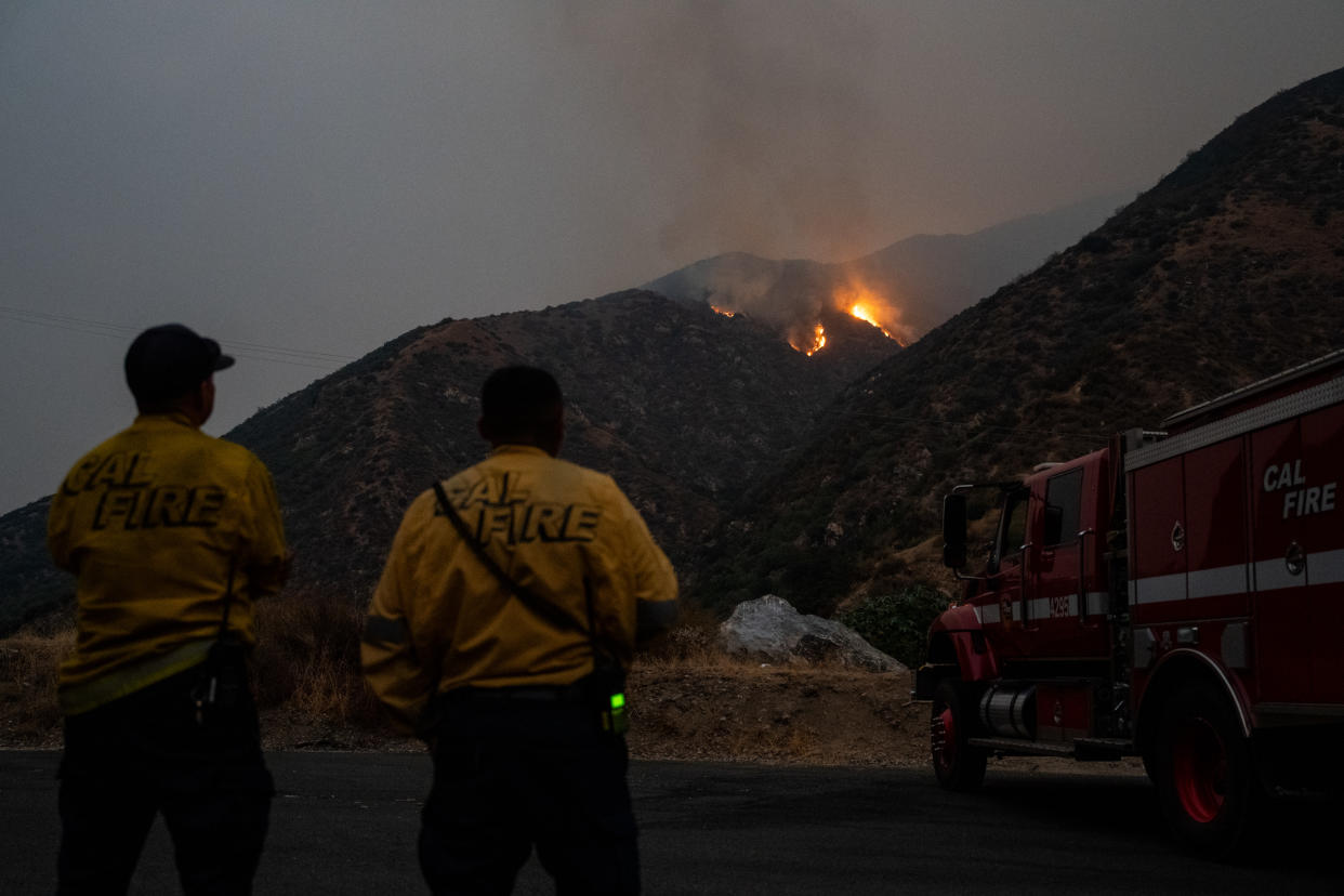 Firefighters look on as a fire grows.