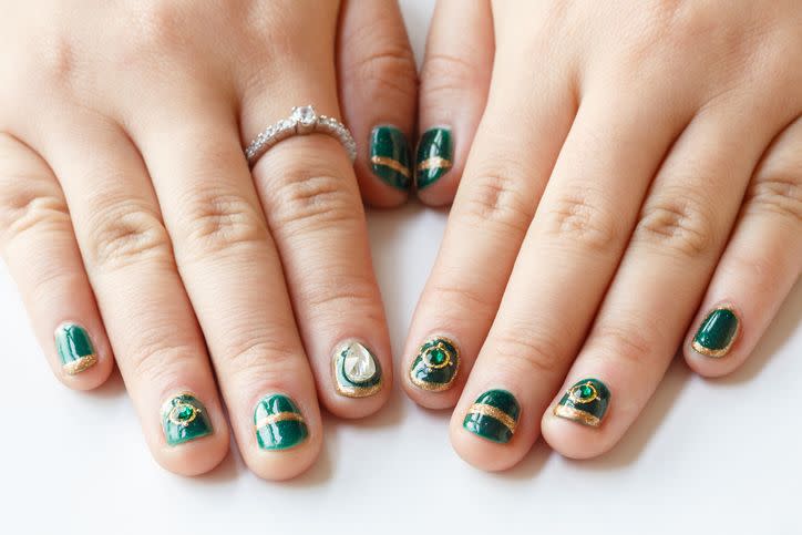 a pair of girls hands with a green and gold shiny manicure with nail jewels
