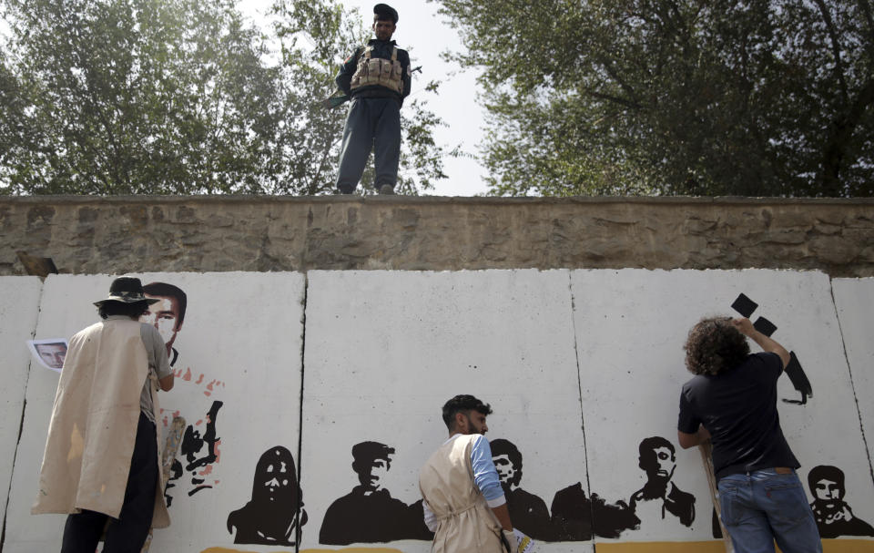 A policeman stands guard as artists from ArtLords organization paint a mural of journalists who have been killed during the year of 2018, in Kabul, Afghanistan, Tuesday, Sept. 25, 2018. It's the first in a series of murals planned by Amnesty International and the Artlords collective to highlight the work of Afghan activists, teachers, lawyers, students, trade unionists and others. (AP Photo/Massoud Hossaini)