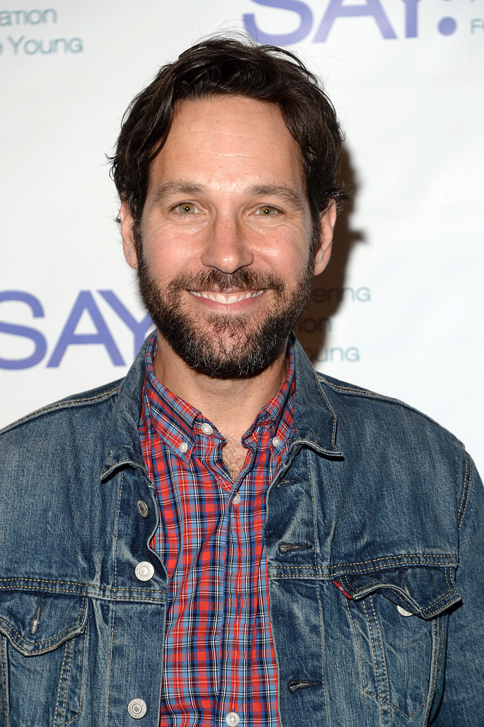 Man smiling in a denim jacket over a plaid shirt at an event