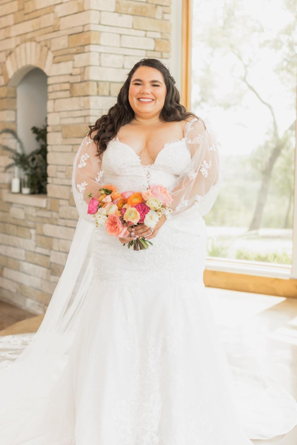 A bride smiles holding a colorful bouquet in front of a fireplace.