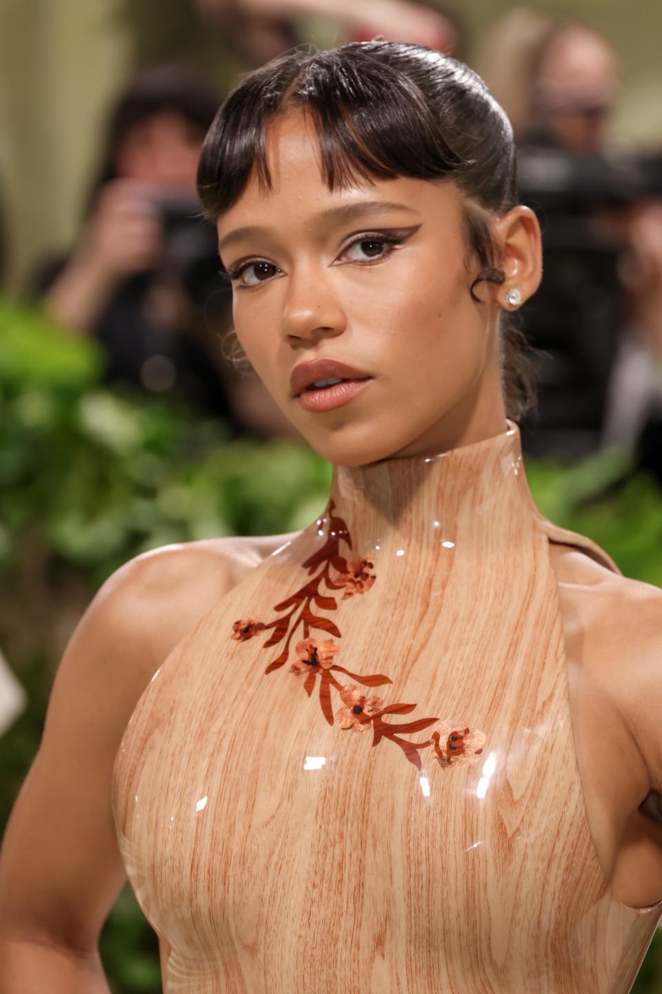 Woman poses in a transparent halter-neck gown with decorative floral embellishments