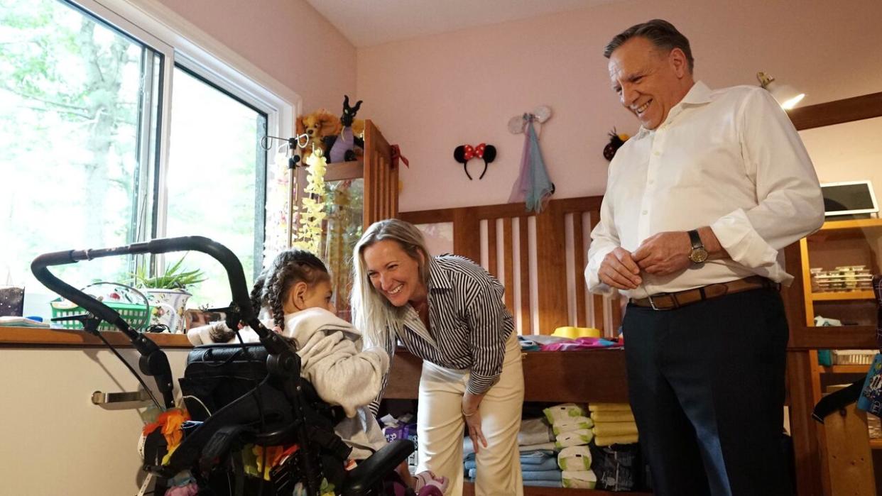 Soulanges MNA Marilyne Picard stands before her daughter Dylane, who has a congenital disease which prevents her from walking and speaking, as Premier François Legault looks on.  (Mathieu Potvin/Radio-Canada - image credit)