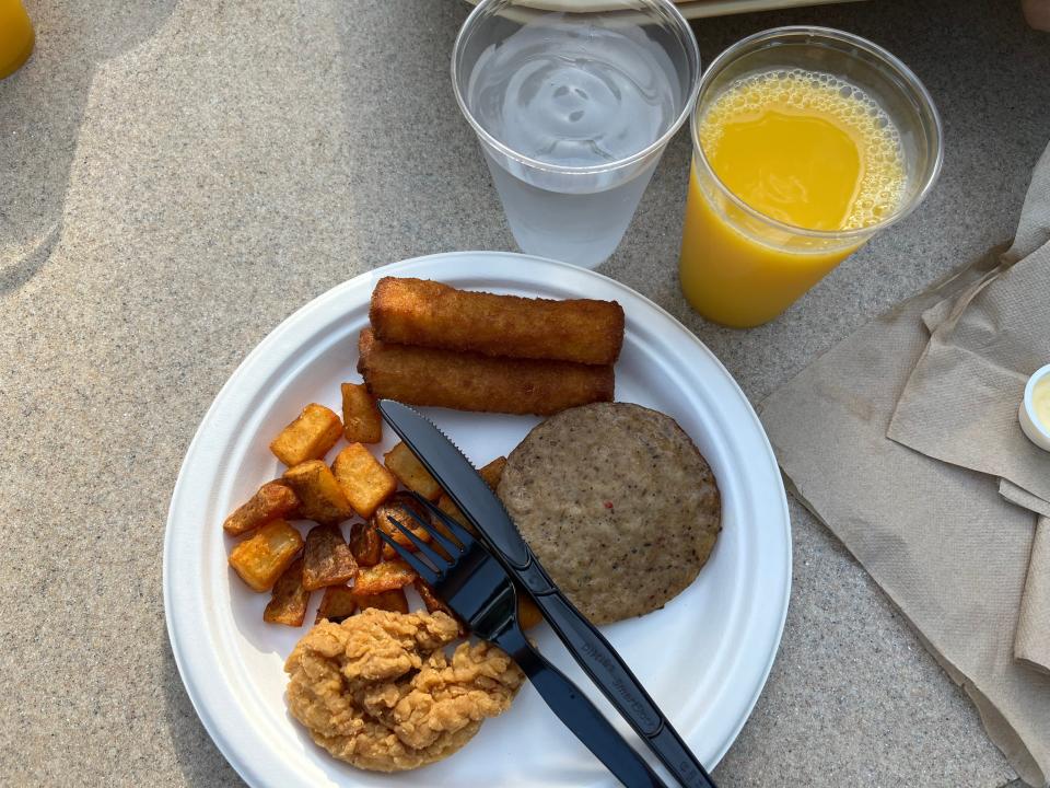 plate of breakfast food and cups of orange juice and water on a concrete floor at discovery cove