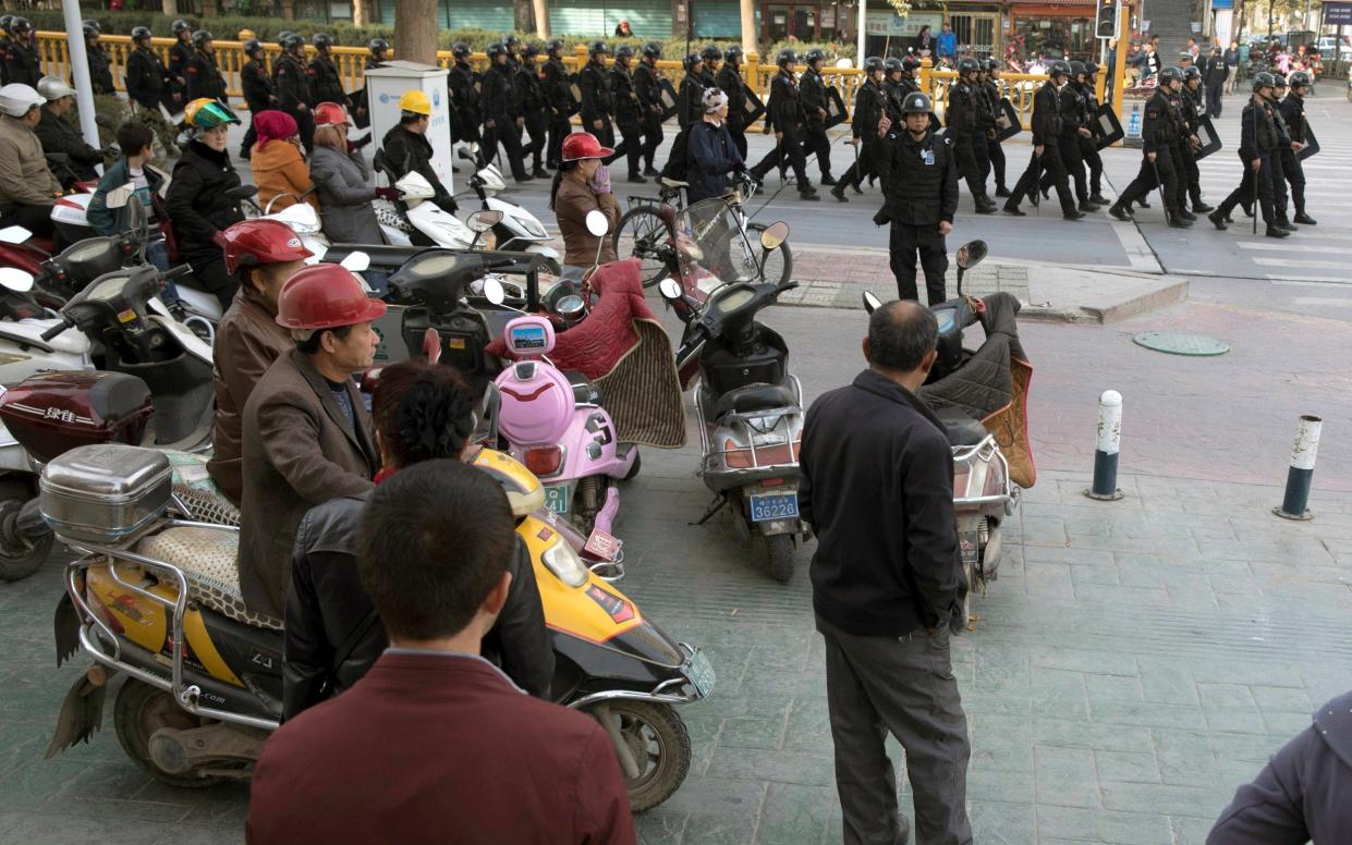 Residents watch a convoy of security personnel in a show of force through central Kashgar in western China's Xinjiang region, November 2017 - AP