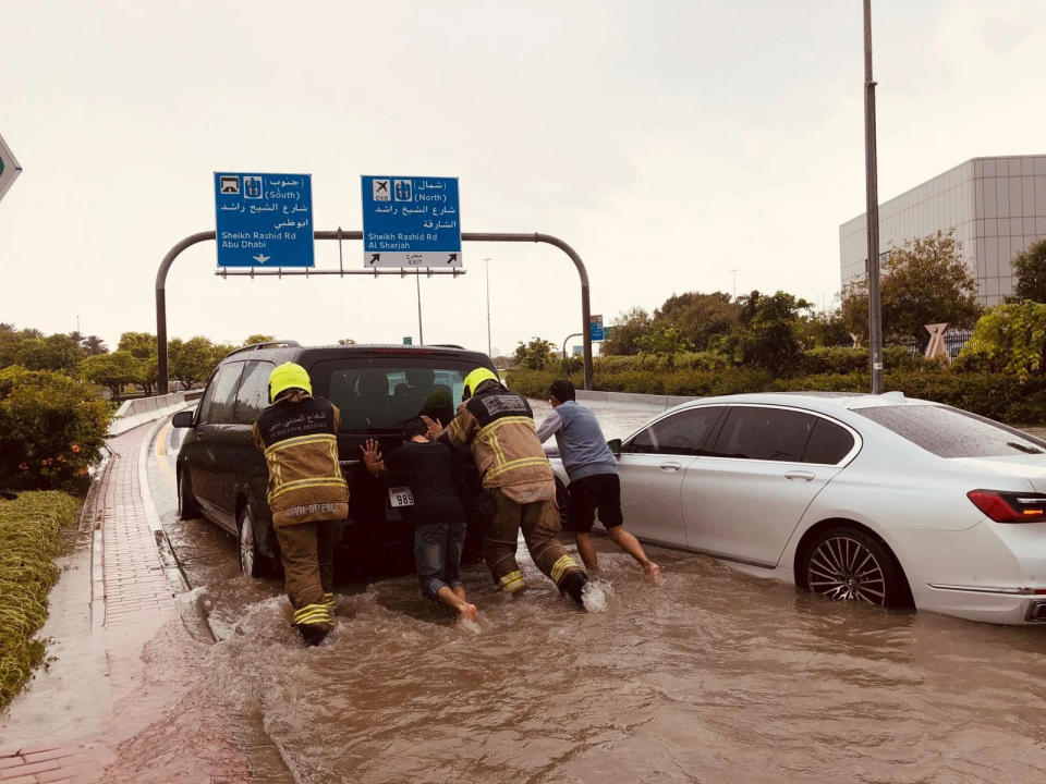 Emergency crews, a passenger and the driver try to push a stalled car out of the roadway.