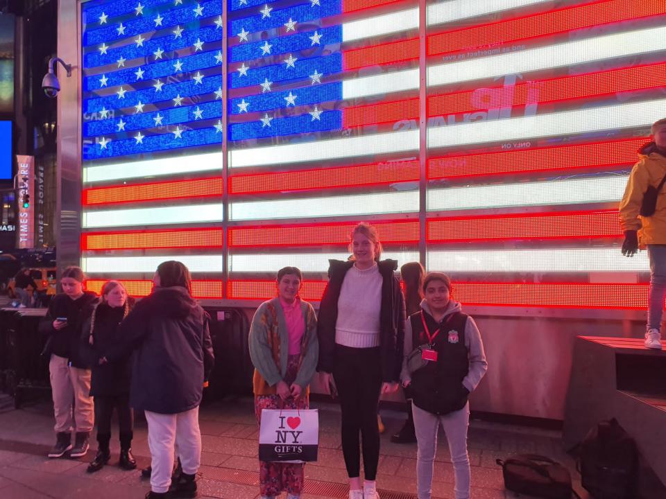 3 students posing in front of an American flag