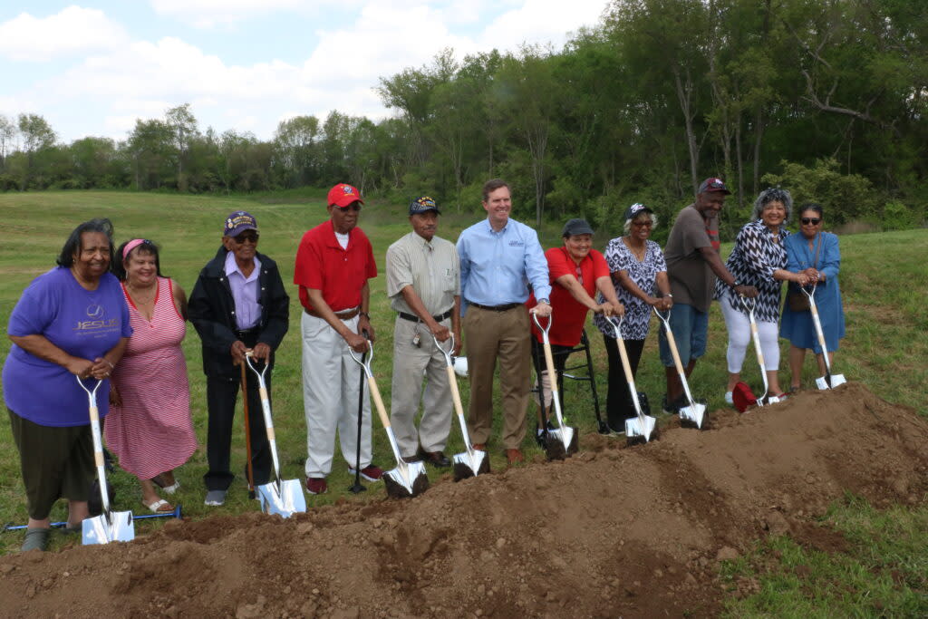 A group of people stand by a pile of dirt holding shovels.