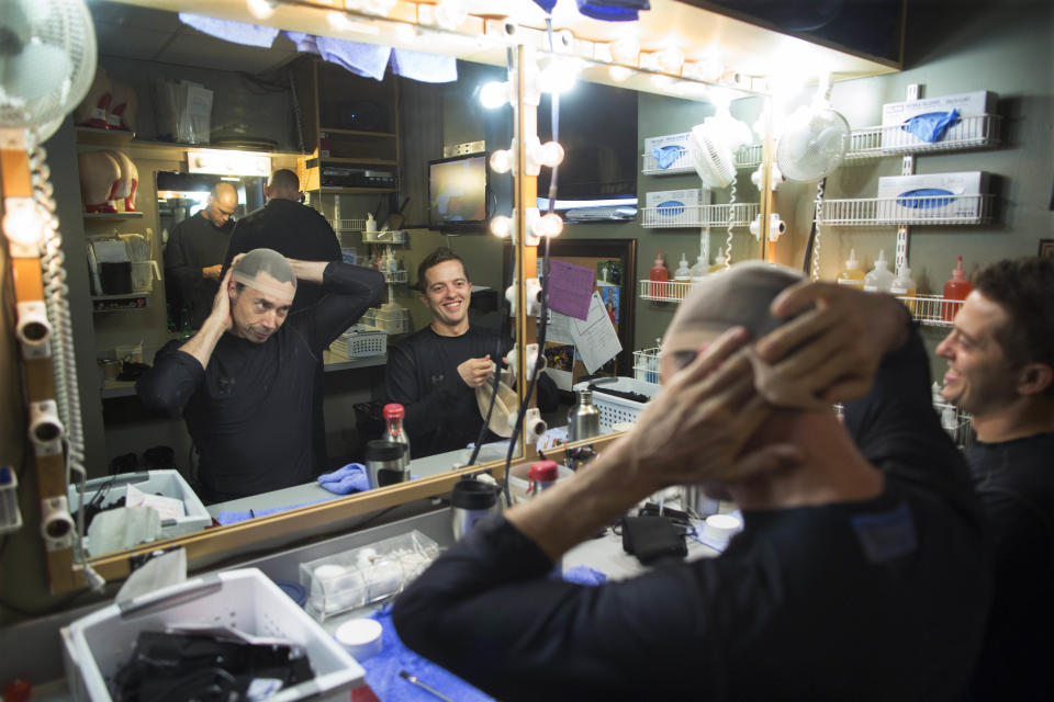 In this July 10, 2013, photograph, current members of the Blue Man Group, from left reflected in the mirror, Scott Bishop, Eric Gebow and Collin Batten prepare to get into character backstage at the Briar Street Theatre. The Blue Man Group recently held open auditions in Chicago hoping to add to their recently expanded shows throughout the world. (AP Photo/Scott Eisen)