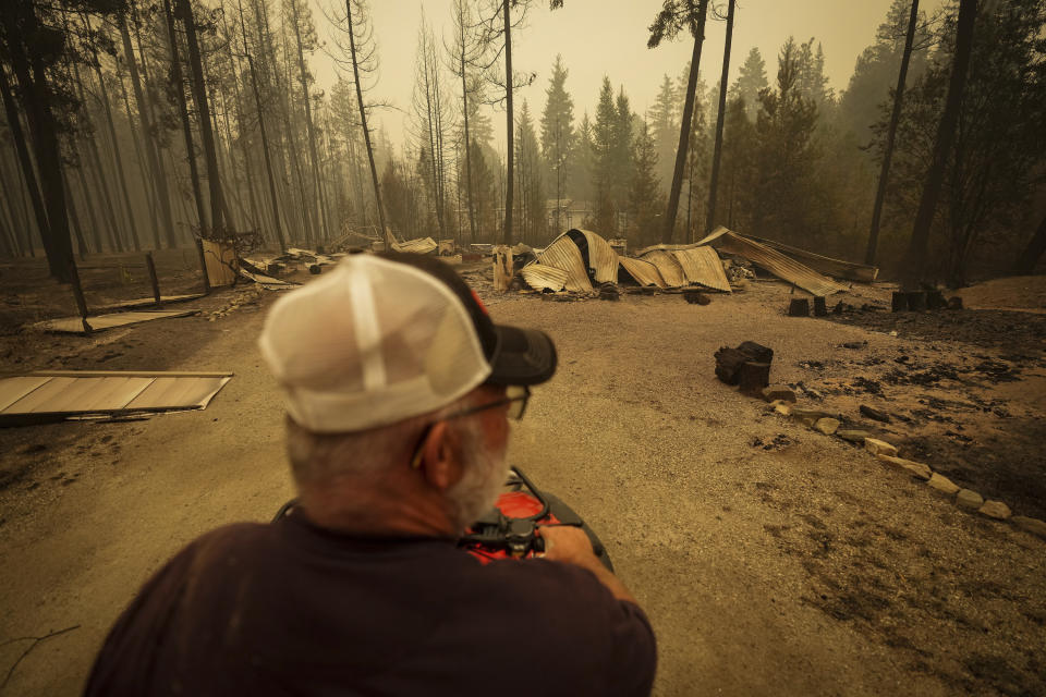 Trevor Manzuik, who was evacuated from his home, views a property that was destroyed by the Lower East Adams Lake wildfire while using an all-terrain vehicle to check on his neighbors after returning home by boat, in Scotch Creek, British Columbia, on Sunday, Aug. 20, 2023. (Darryl Dyck/The Canadian Press via AP)