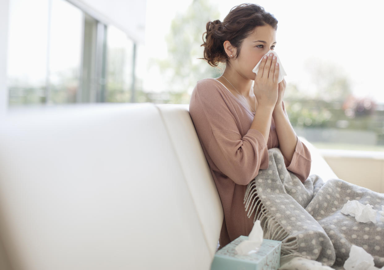 sick woman blowing her nose on a couch with a cold xbb 