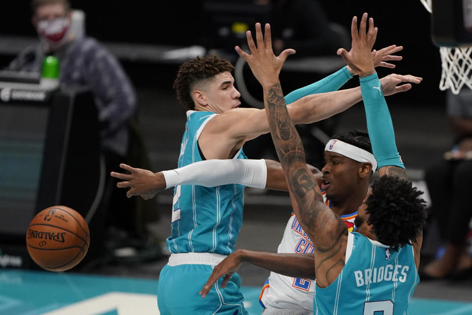 Oklahoma City Thunder guard Shai Gilgeous-Alexander passes the ball between Charlotte Hornets guard LaMelo Ball, left, and forward Miles Bridges during the first half of an NBA basketball game in Charlotte, N.C., Saturday, Dec. 26, 2020. (AP Photo/Chris Carlson)