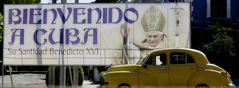 A vintage car drives past a billboard welcoming Pope Benedict XVI, just days before his arrival, in Havana, Cuba, Wednesday March 21, 2012. Pope Benedict XVI's trip to Latin America takes him to the region's most Catholic country; Mexico, and then Cuba, where churches are mostly empty and until the 1990s, believers were barred from the Communist Party. (AP Photo/Javier Galeano)