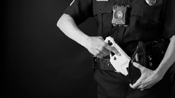 A police officer puts an Axon Enterprise TASER stun gun in a holster.