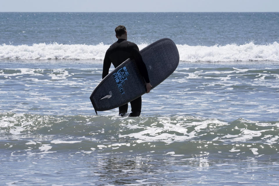 Dan Fischer, of Newport, R.I., walks into the ocean with his surfboard at Easton's Beach, in Newport, Wednesday, May 18, 2022. Fischer, 42, created the One Last Wave Project in January 2022 to use the healing power of the ocean to help families coping with a loss, as it helped him following the death of his father. Fischer places the names onto his surfboards, then takes the surfboards out into the ocean as a way to memorialize the lost loved ones in a place that was meaningful to them. (AP Photo/Steven Senne)
