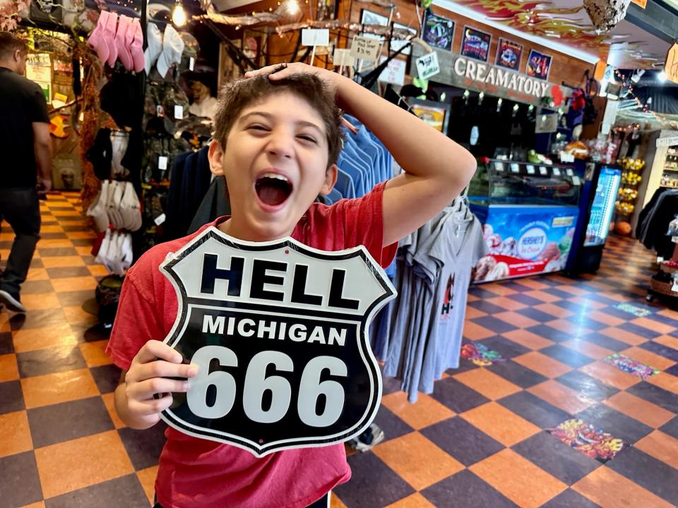 The author's son holding a Hell Michigan 666 road sign and laughing in a souvenir shop 