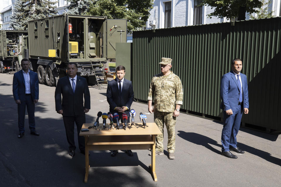 Ukrainian President Volodymyr Zelenskiy, center, speaks during the presentation new experimental military modular equipment for field in Kiev, Ukraine, Friday, July 19, 2019.Ukraine's president on Friday outlined the details of an impending prisoner swap with Russia, saying that Kiev is willing to release a jailed Russian journalist in exchange for a Ukrainian film director. (Ukrainian Presidential Press Office via AP)