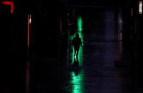 A person is silhouetted against the reflections of the lights of two open pharmacies on the paviment in the empty La Bola street during partial lockdown as part of a 15-day state of emergency to combat the coronavirus disease (COVID-19) outbreak in Ronda