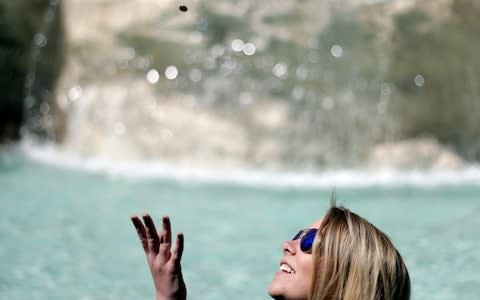 A woman tosses a coin into the Trevi fountain in Rome. Legend has it that tossing a coin over one's shoulder into the fountain ensures a return visit - Credit: Gregorio Borgia/AP