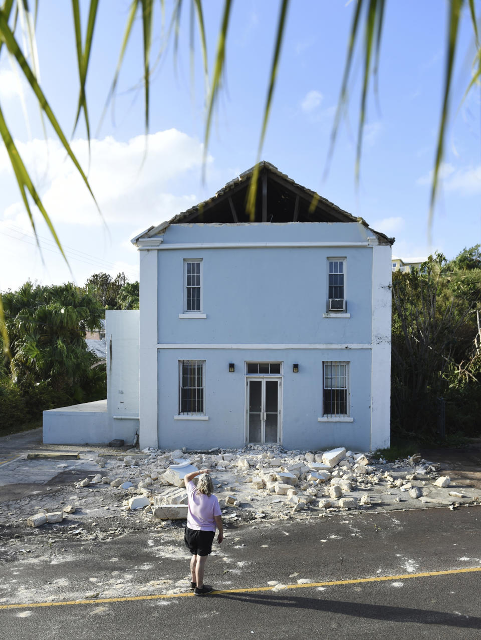 A woman looks up at a building damaged by Hurricane Humberto in Blue Hole Park, Bermuda, Thursday, Sept. 19, 2019. Humberto blew off rooftops, toppled trees and knocked out power but officials said Thursday that the Category 3 storm caused no reported deaths. (AP Photo/Akil J. Simmons)