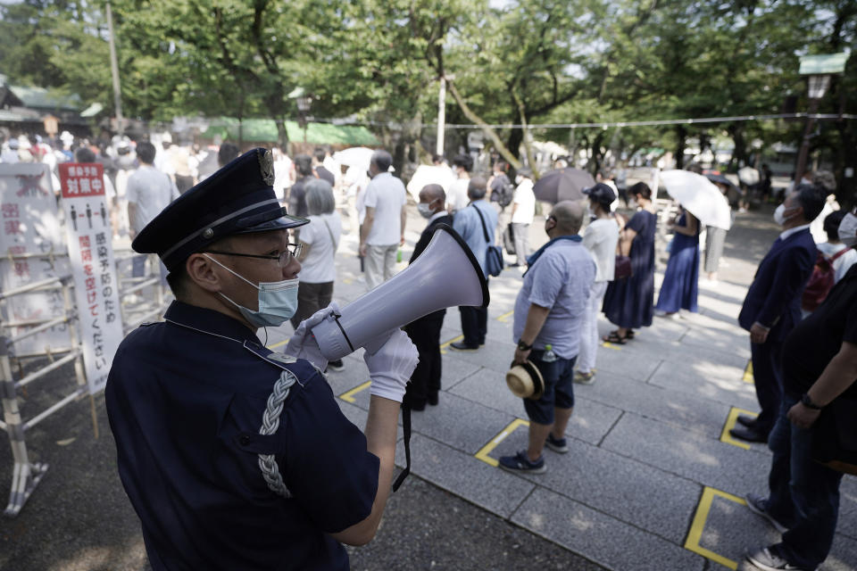 A security guard controls visitors queue to enter Yasukuni Shrine Saturday, Aug. 15, 2020, in Tokyo. Japan marked the 75th anniversary of the end of World War II. (AP Photo/Eugene Hoshiko)