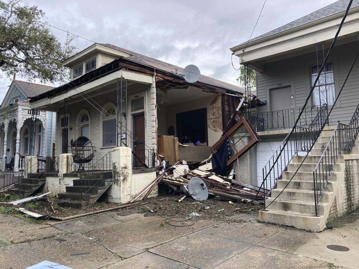 House with a section of wall missing and debris scattered about the sidewalk.