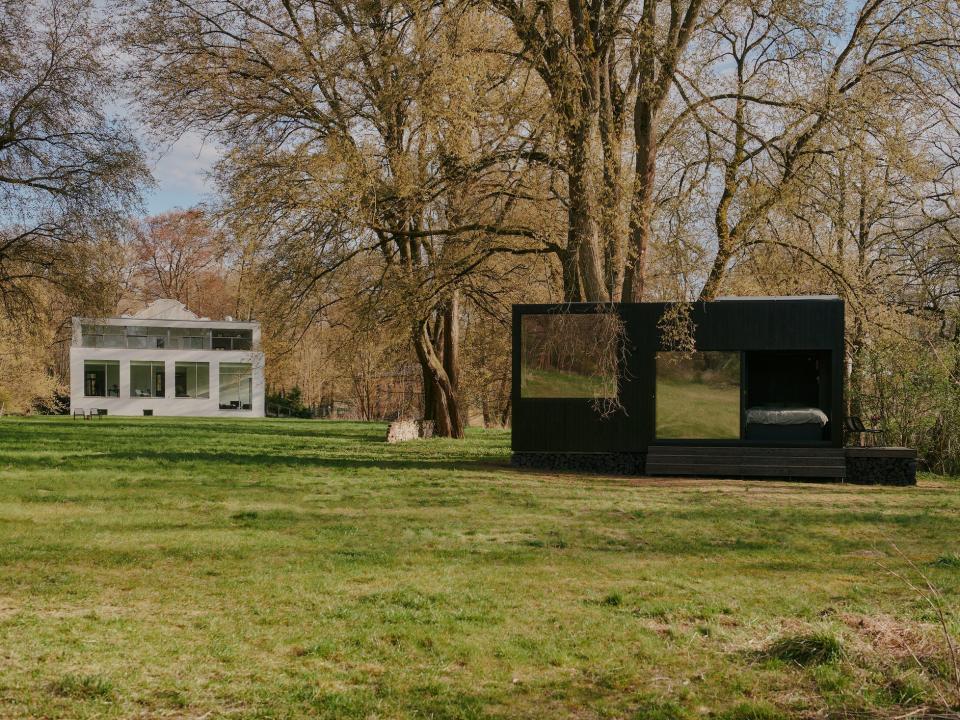 A Raus cabin in nature surrounded by trees and a nearby home