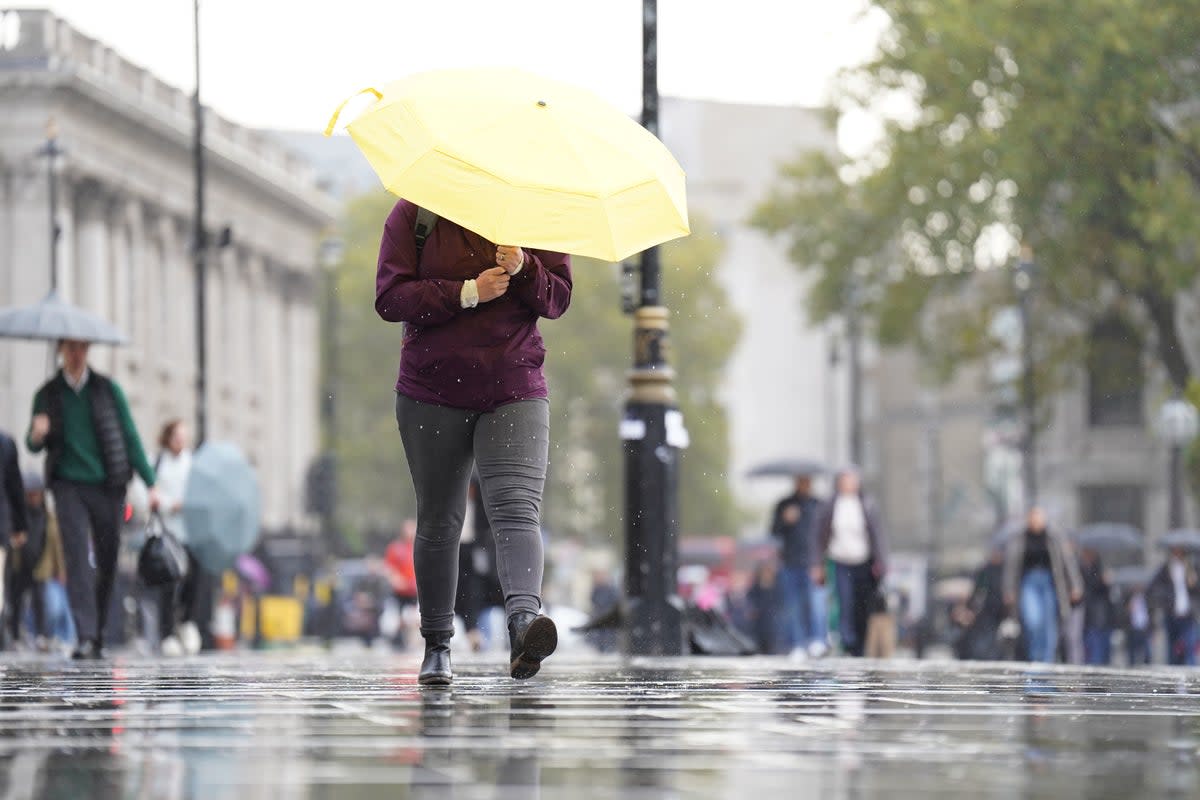 A woman shelters from the wet weather beneath an umbrella near Trafalgar Square (PA)