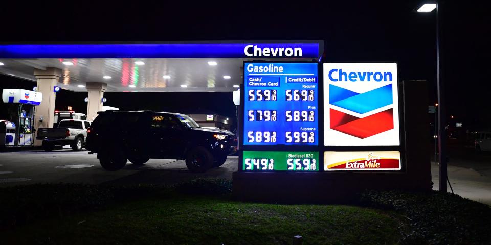 A sign at a Chevron gas station at night displays high prices.