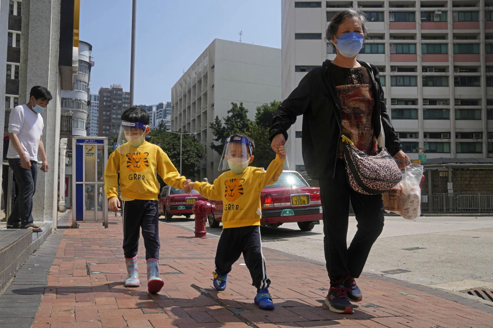 FILE - A woman and children wearing face masks and shields walk on a street in Hong Kong on March 4, 2022. The fast-spreading omicron variant is overwhelming Hong Kong, prompting mass testing, quarantines, supermarket panic-buying and a shortage of hospital beds. Even the morgues are overflowing, forcing authorities to store bodies in refrigerated shipping containers. (AP Photo/Kin Cheung, File)