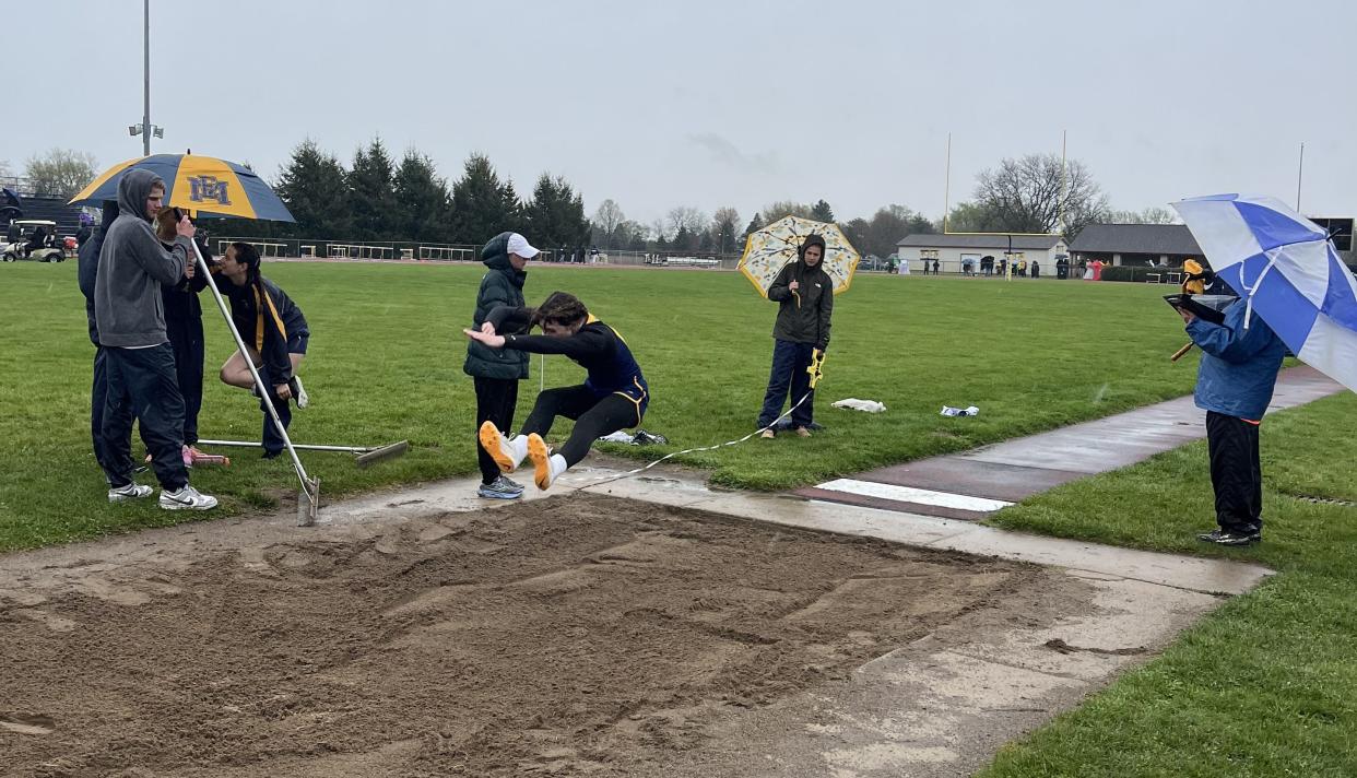 Meet officials huddle under umbrellas as Rylie DeSilvis long jumps for Whiteford during meets against Erie Mason and Summerfield on Tuesday, March 23, 2024.