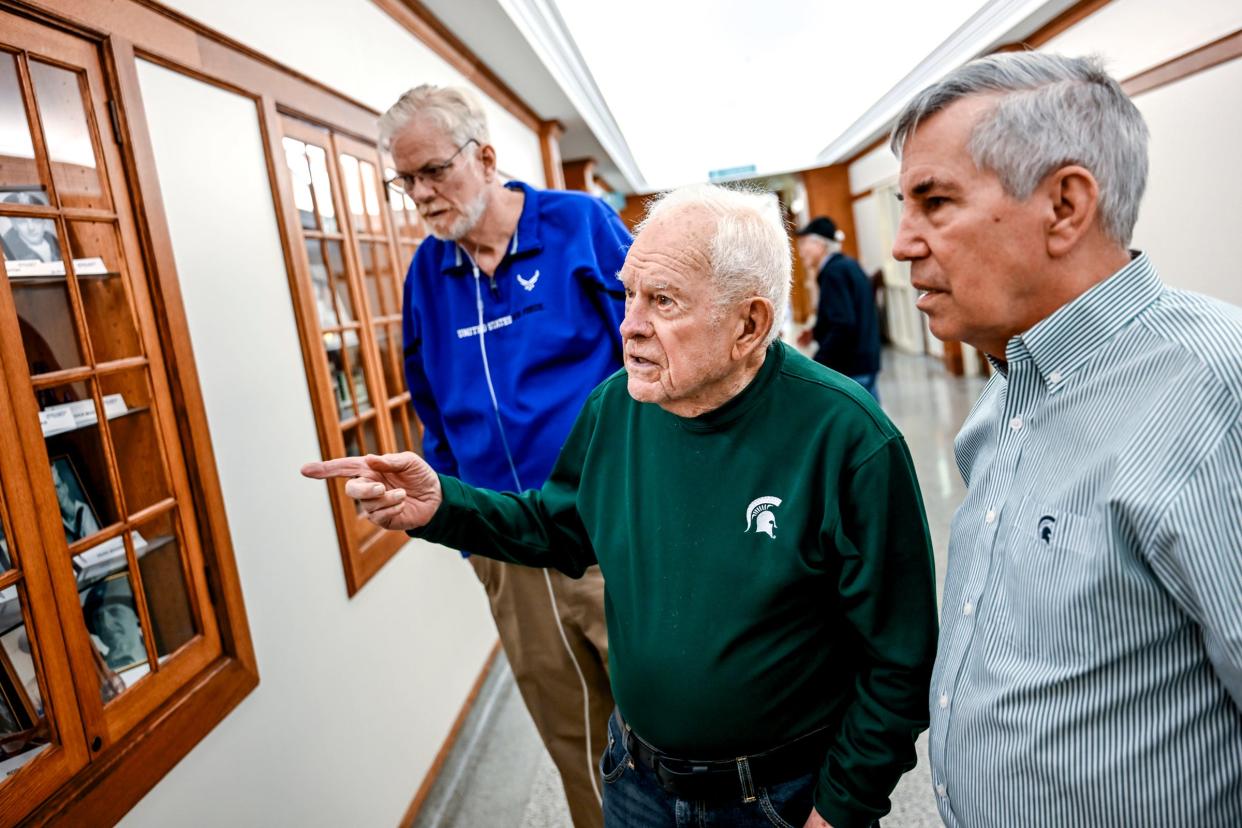 Richard Masters, center, who served in the U.S. Navy in World War II, looks at a display of other community members who served in the war with his son Greg Masters and nephew Jay Masters on Tuesday, April 30, 2024, at the Hannah Community Center in East Lansing.