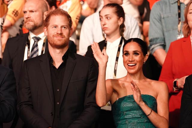 Harry and a waving Meghan stand in the audience at the Invictus Games in Dusseldorf last year 