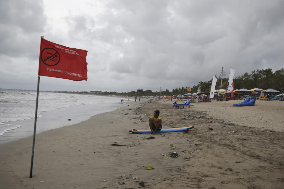 A man sits on a surfboard at Kuta beach on the popular tourist island of Bali, Indonesia, Thursday, Jan. 19, 2023. A hoped-for boom in Chinese tourism in Asia over next week's Lunar New Year holidays looks set to be more of a blip as most travelers opt to stay inside China if they go anywhere. (AP Photo/Firdia Lisnawati)