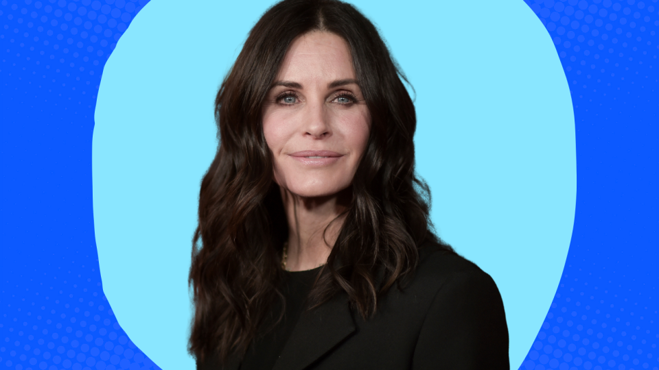 Courteney Cox wearing a black blazer on a blue background