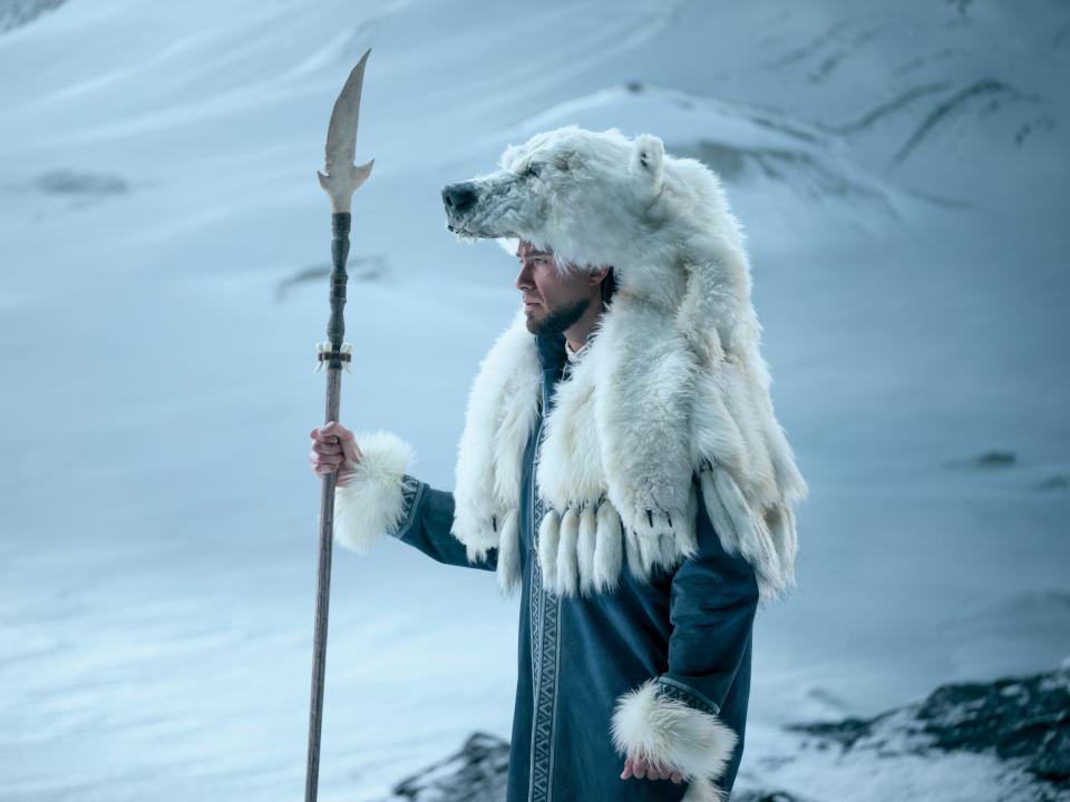 avatar kuruk in avatar the last airbender. he's holding a spear, wearing a blue overcoat, and has a polar bear fur over his head