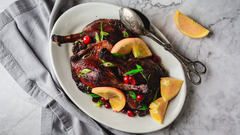 Roasted duck legs on white plate, tongs and napkin