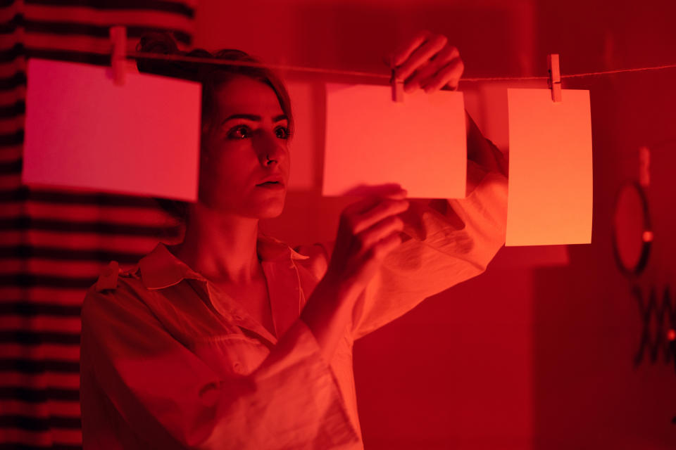 Woman in a photo darkroom examines photos on a drying line