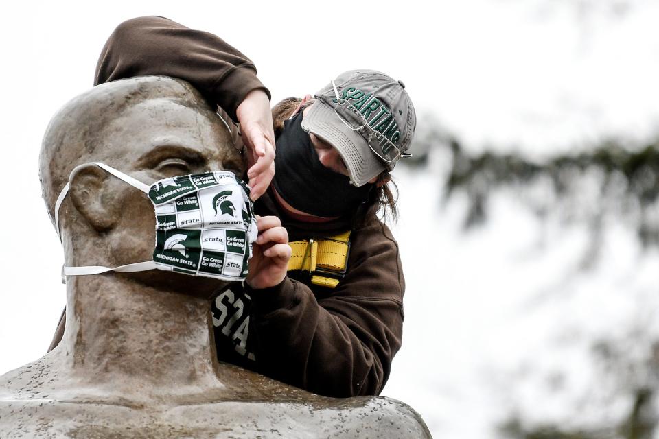 Michigan State University utility worker Kimberly Consavage adjusts a mask on the Sparty statue on April 22, 2020, on the campus in East Lansing.