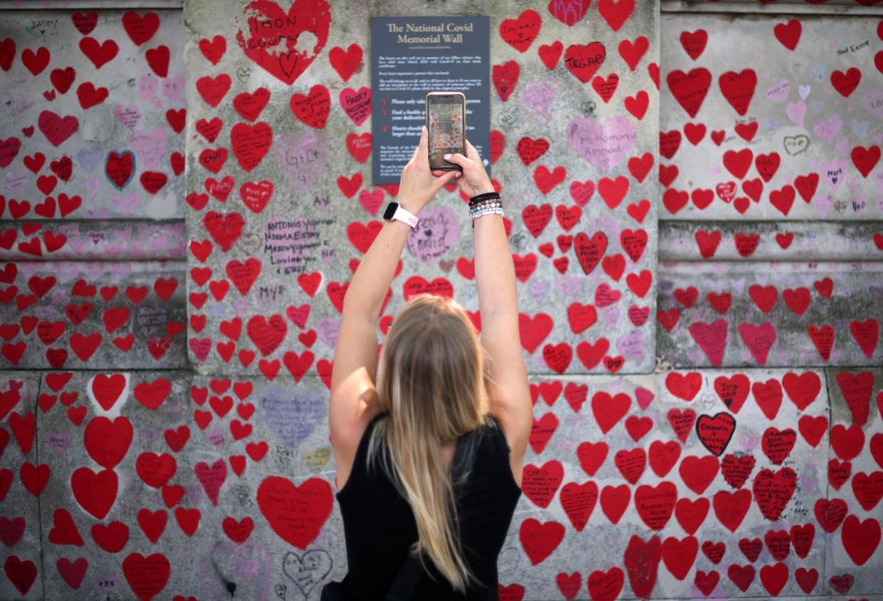 A person takes a photograph of the plaque on the National Covid Memorial Wall, dedicated to those who lost their lives to Covid-19, on the embankment on the south side of the River Thames in London on June 13, 2023. An inquiry probing the UK government's handling of the coronavirus pandemic kicked off Tuesday with the investigation mired in controversy even before the first witness is called. The inquiry chair, retired senior judge Heather Hallett, has called for ex-prime minister Boris Johnson's unredacted WhatsApp messages and notebooks to be handed over, prompting a legal challenge from the government of his successor Rishi Sunak. (Photo by Daniel LEAL / AFP) (Photo by DANIEL LEAL/AFP via Getty Images)