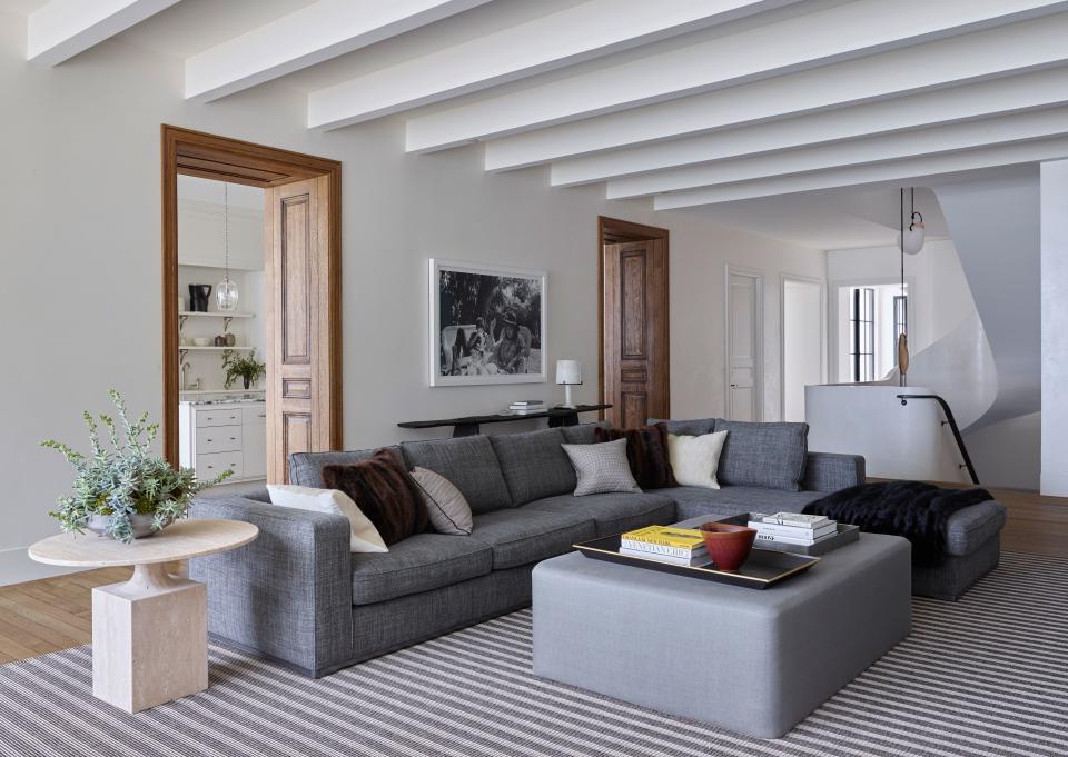 A Maxalto sectional sofa upholstered in a Rogers & Goffigon fabric creates a base for a travertine side table by Vincent Dupont-Rougier for the Delcourt Collection, a rug by Mitchell Denberg, and a custom ottoman covered in a Pierre Frey glazed linen.