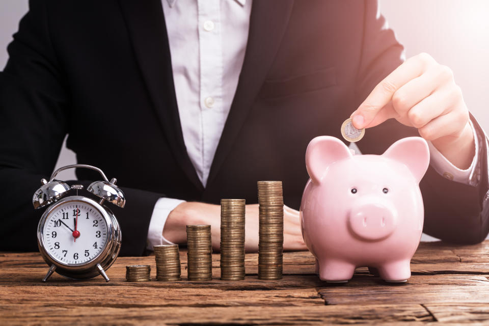 A person in a suit putting coins into a piggy bank.