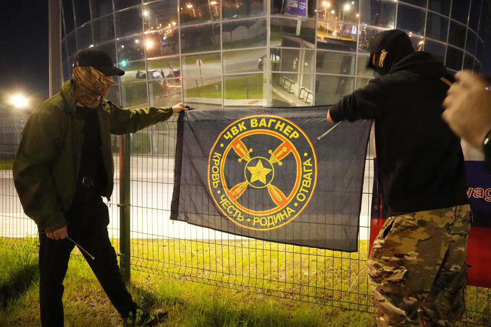 Men hang a flag of 'PMC Wagner' at an informal memorial next to the former 'PMC Wagner Centre' in St. Petersburg, Russia, early Thursday, Aug. 24, 2023. Russia's civil aviation agency says mercenary leader Yevgeny Prigozhin was aboard a plane that crashed north of Moscow. (AP Photo/Dmitri Lovetsky)